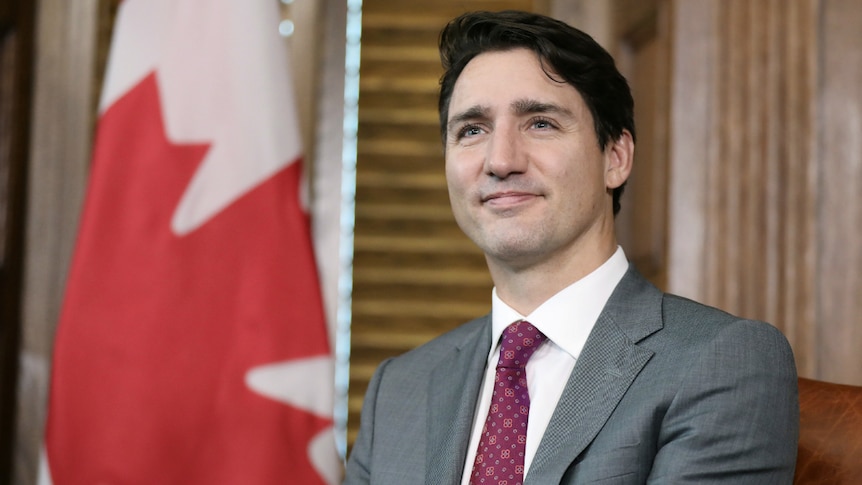 Prime Minister Justin Trudeau siting next to a Canadian flag.