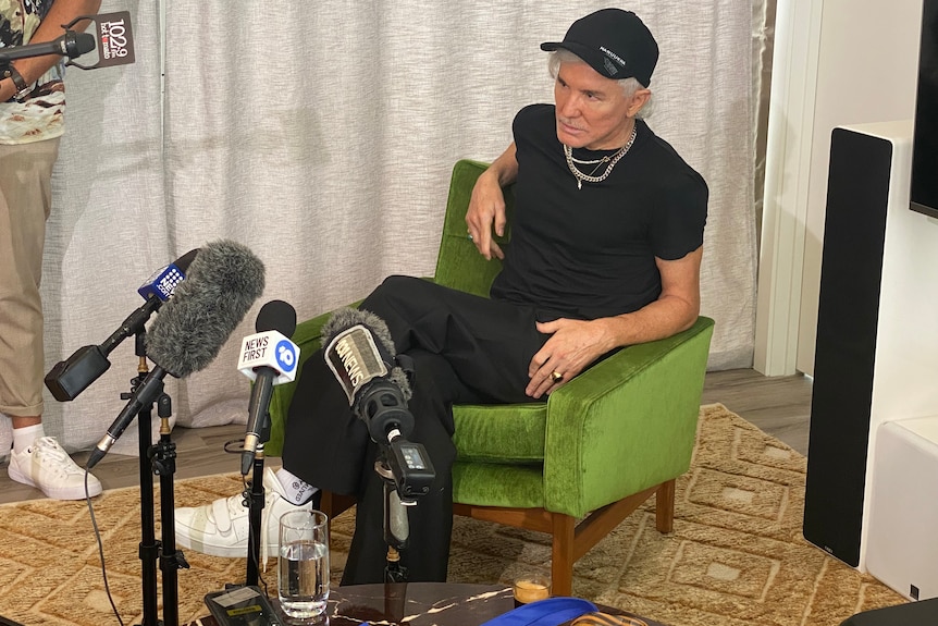 Baz Luhrmann sits in a green chair doing an interview