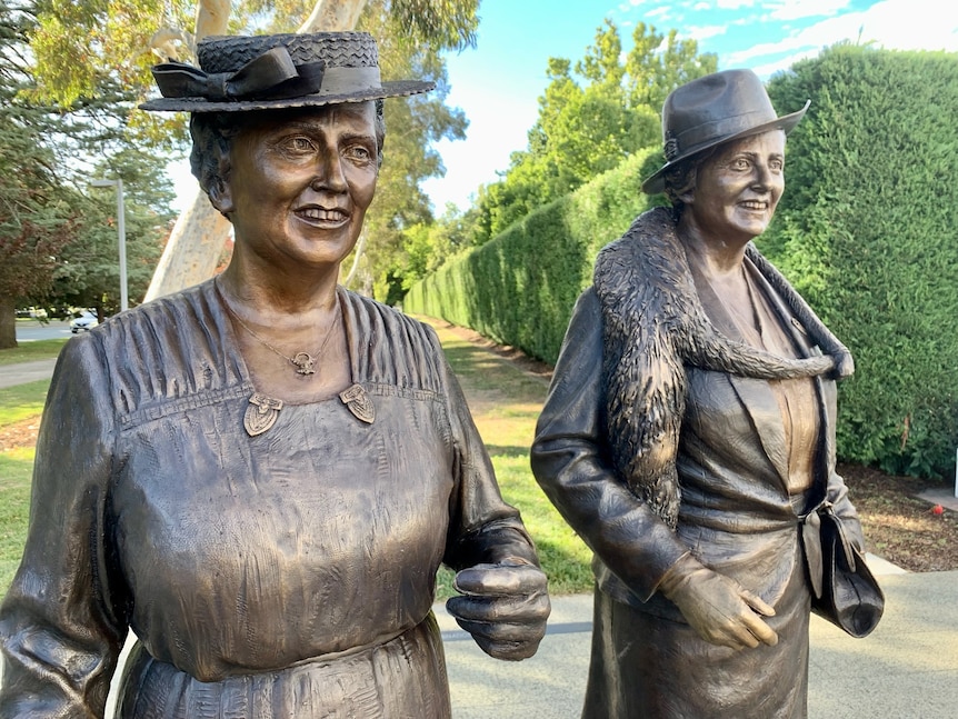 Bronze life-size statues of two women in hats smiling
