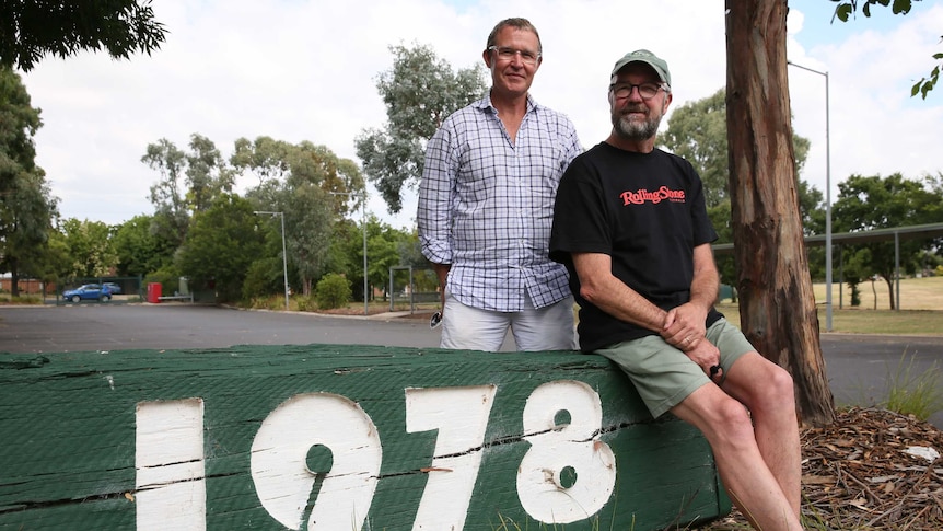 Two men next to original high school sign