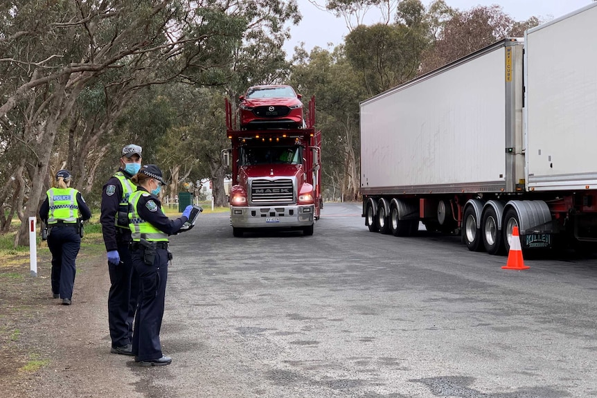 Three police officers standing beside two trucks on a road