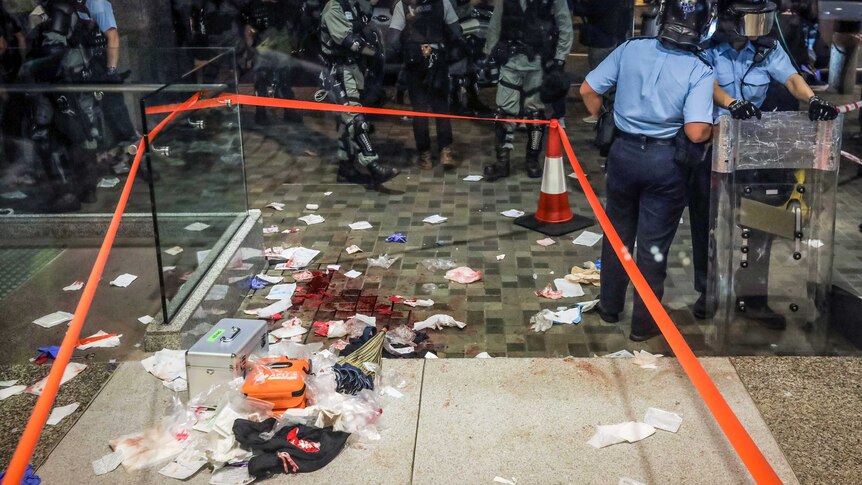 Hong Kong police stand around the perimeter of a cordoned-off crime scene where blood and debris are still on the floor.