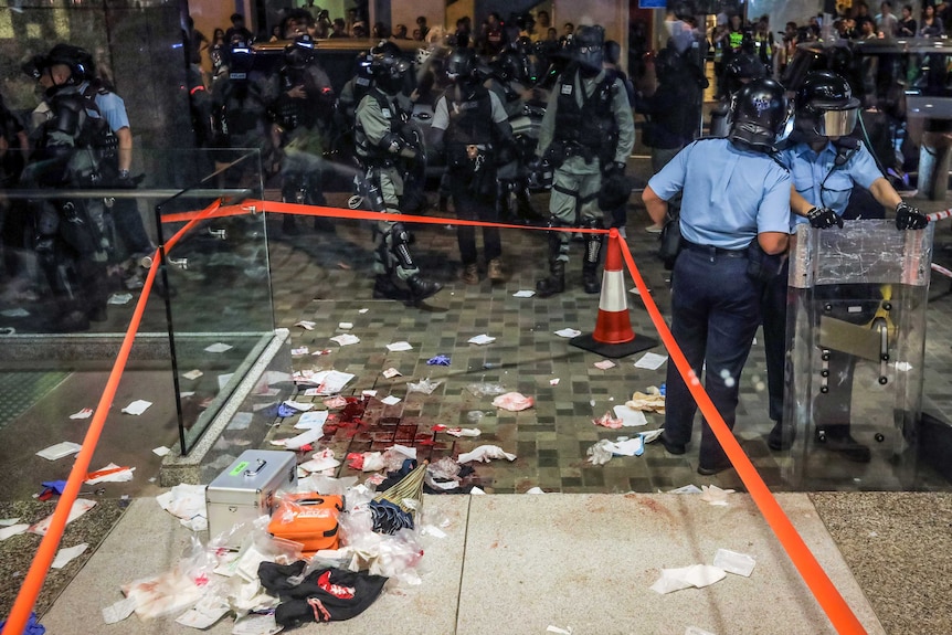 Hong Kong police stand around the perimeter of a cordoned-off crime scene where blood and debris are still on the floor.