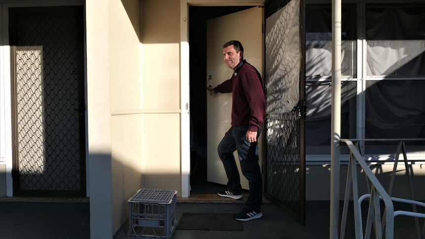 Man smiles as he opens the door of a house