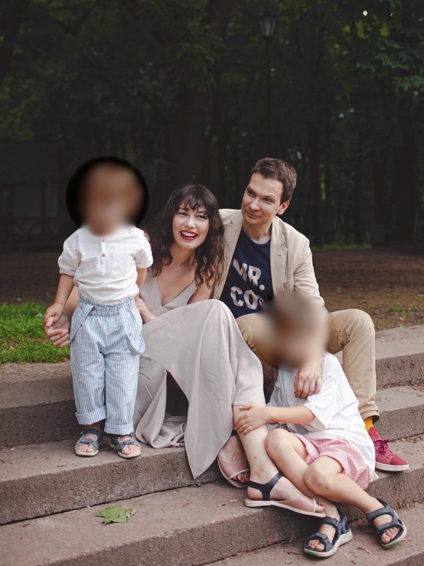 Young couple Elena and Evgeny sitting on steps and smiling with their two kids.