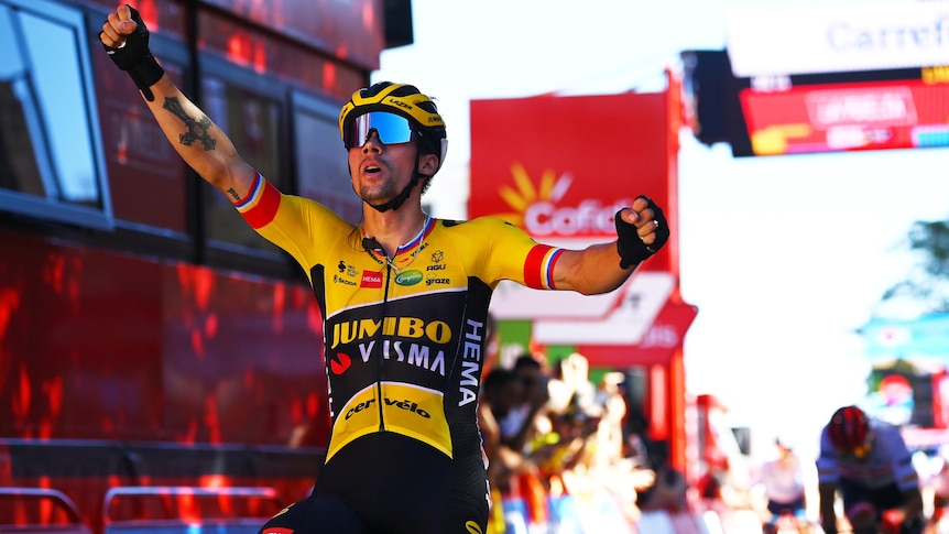 A cyclist in a yellow and black jersey raises his arms high in triumph as he rolls over the line to win a stage of the Vuelta.