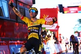 A cyclist in a yellow and black jersey raises his arms high in triumph as he rolls over the line to win a stage of the Vuelta.