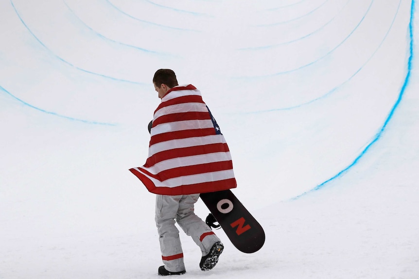 Shaun White walks alone in the halfpipe with the American flag draped over his shoulders.