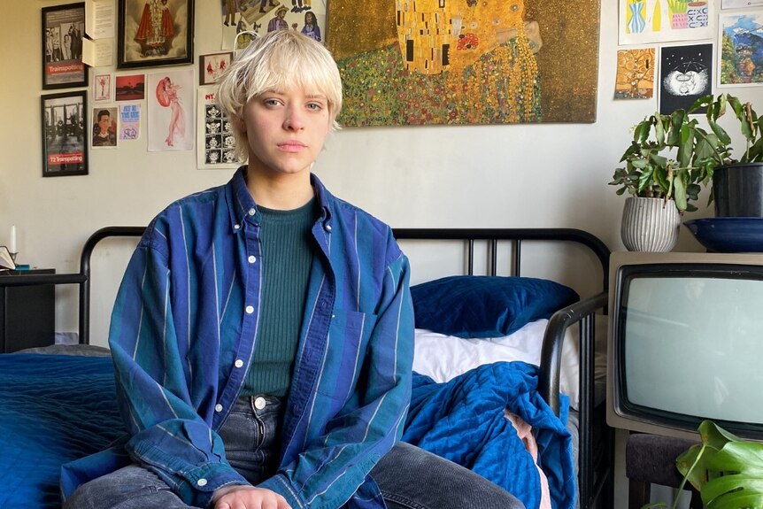 A young white woman with short blonde hair sitting in a bedroom.