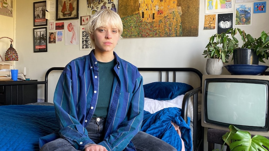 A young white woman with short blonde hair sitting in a bedroom