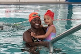 A smiling woman holds a little girl in a swimming pool.