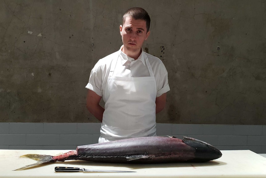 Josh Niland stands at a bench upon which is a large dead fish.