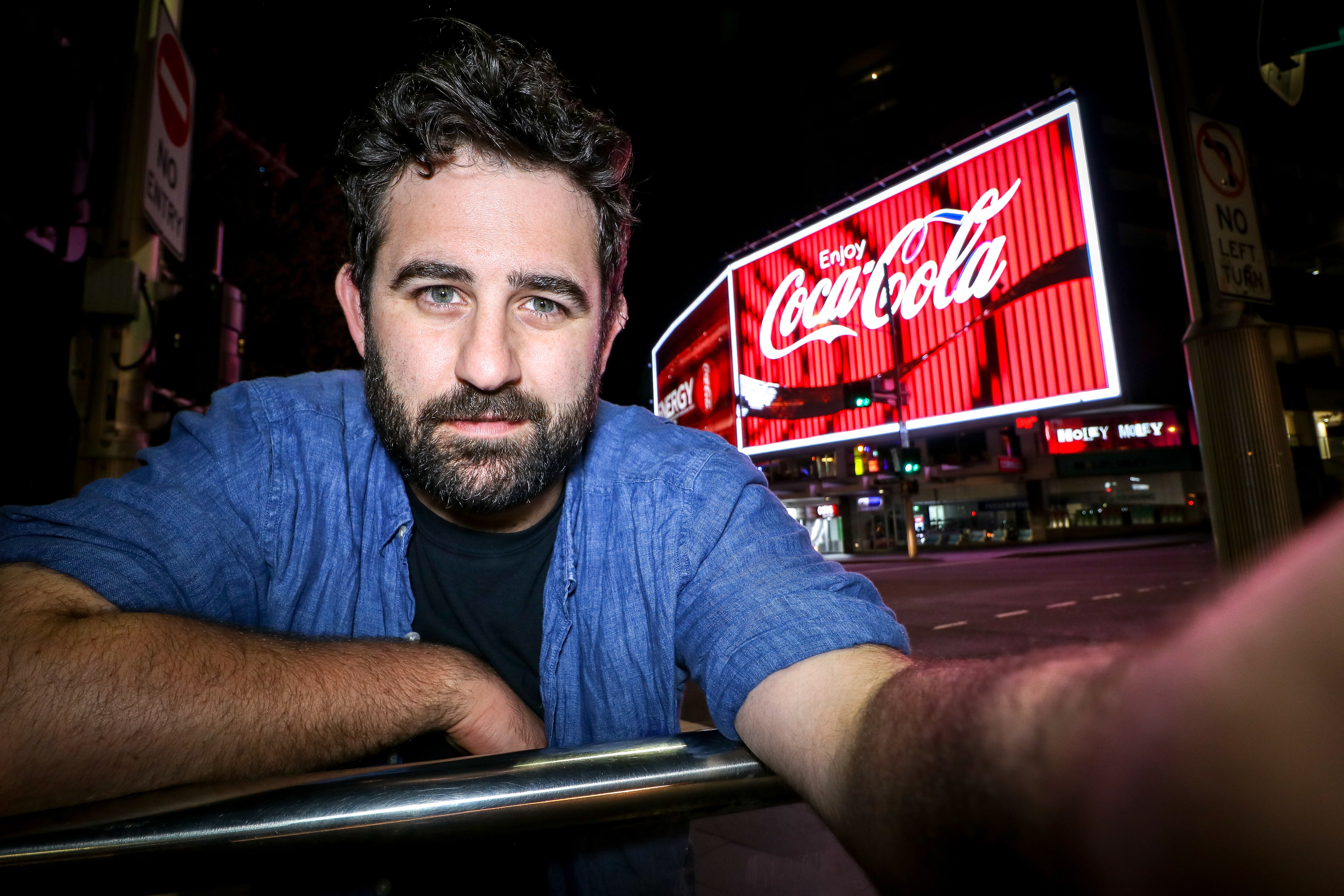 A man grimacing to camera in front of the Coca Cola sign at Kings Cross, Sydney.