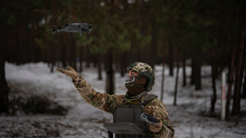 A soldier holds his hand under a drone flying in the air. 