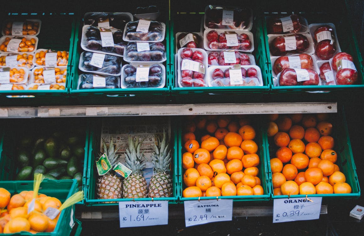 Fruit and vegetables on styrofoam plates wrapped in plastic wrap sit on a grocery store shelf