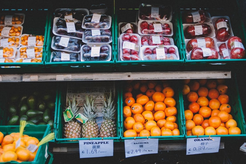 Fruit and vegetables on styrofoam plates wrapped in plastic wrap sit on a grocery store shelf