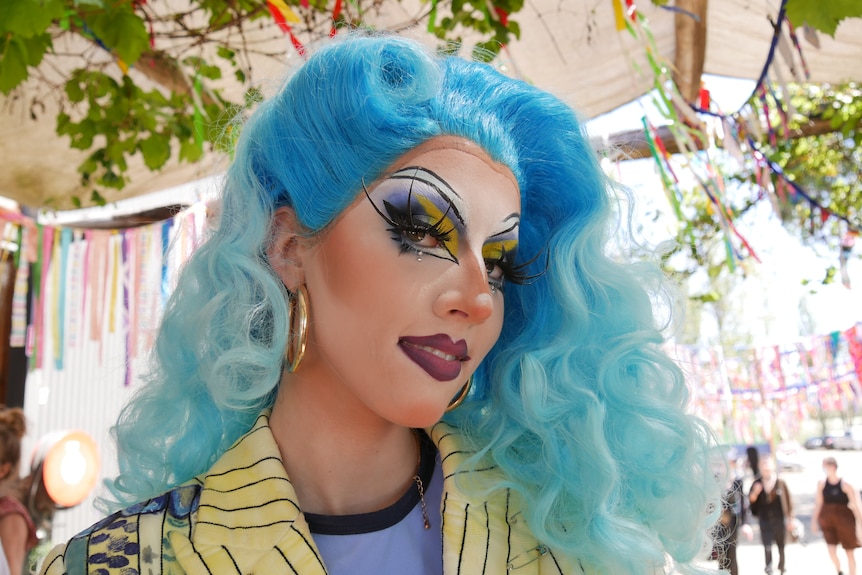 a drag performer with blue hair smiles at the camera