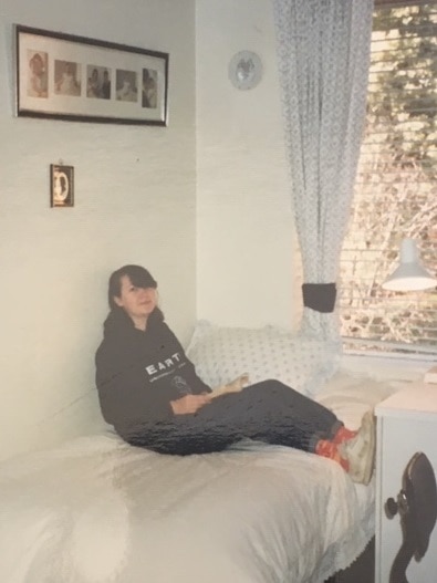 A teenage girl sits on a bed in a pastel-coloured room