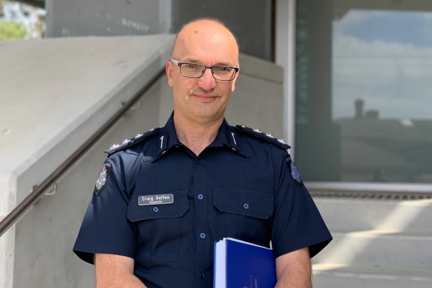 A bald, bespectacled police officer in a dark blue uniform looks benignantly at the camera.