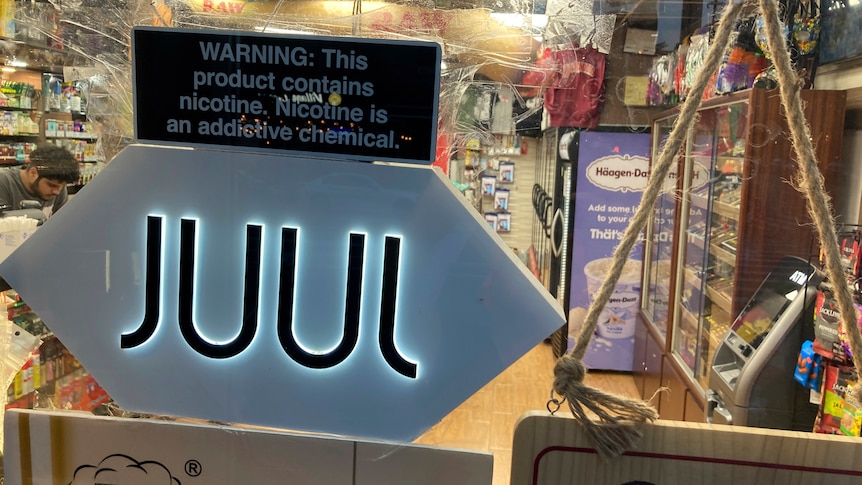 An illuminated Juul sign in the window of a bodega convenience store. 