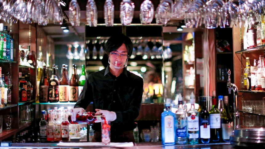 A Japanese man in a black shirt prepares a cocktail in a bar 