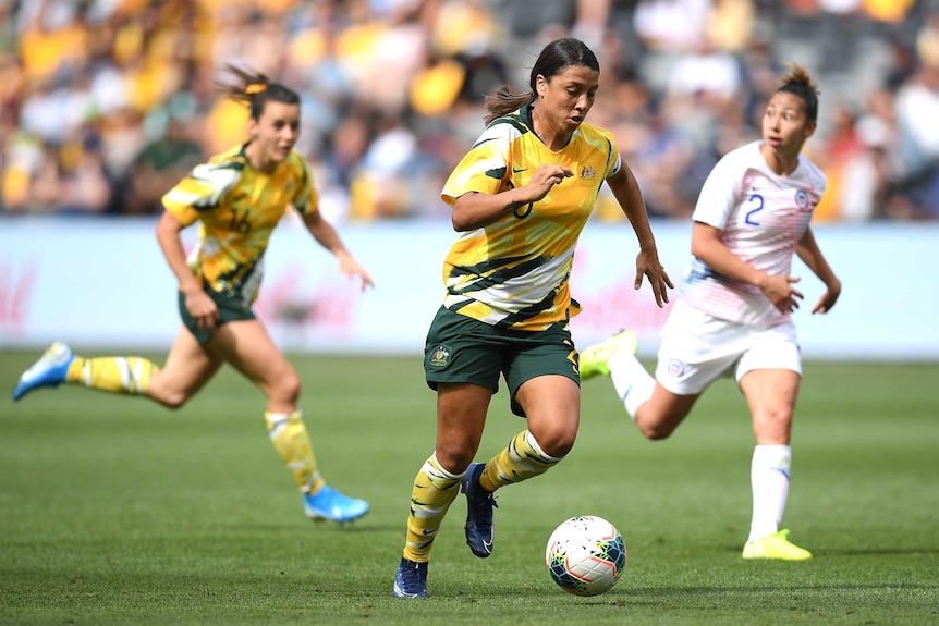 A footballer dribbles with the ball as she runs down the field in an international friendly.