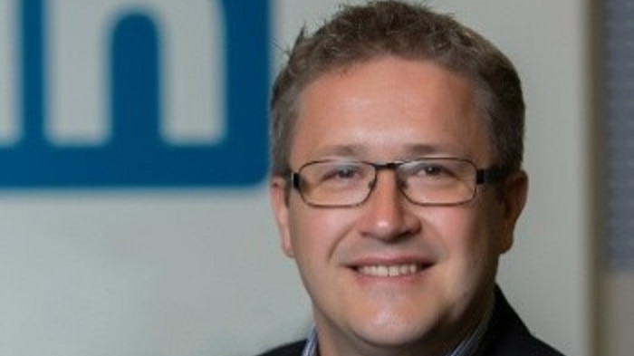 A man wearing a jacket standing in front of the LinkedIn in logo