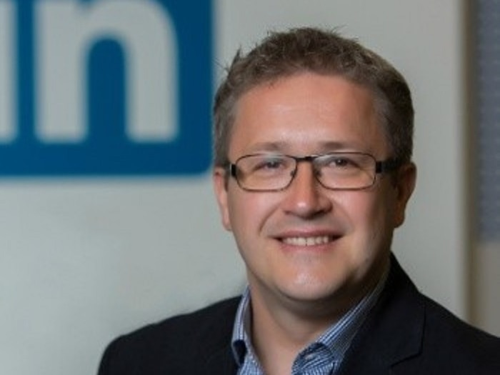 A man wearing a jacket standing in front of the LinkedIn in logo