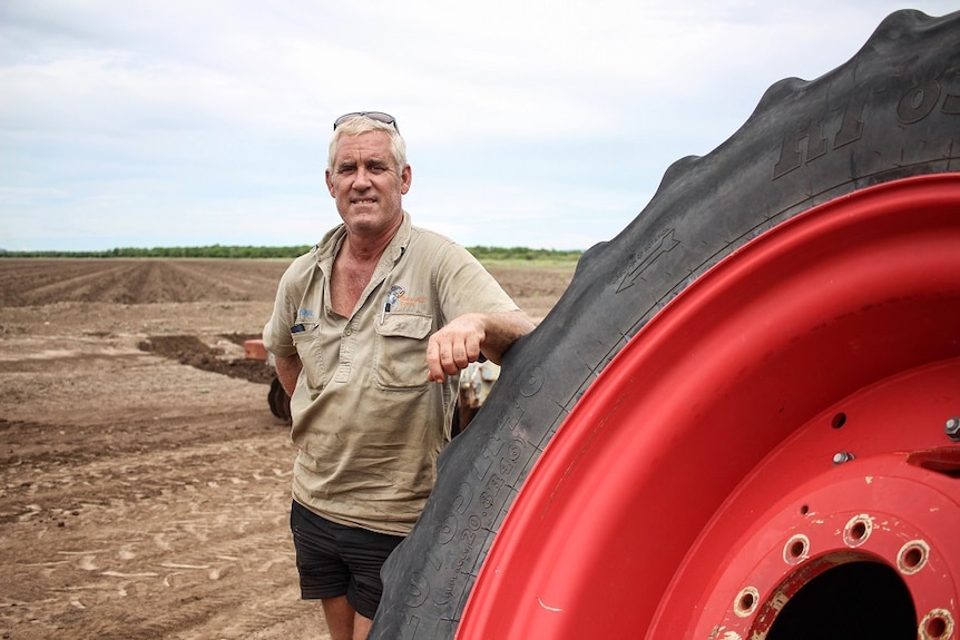A middle-aged man with white hair stands in a paddock, leaning on a tractor tyre.