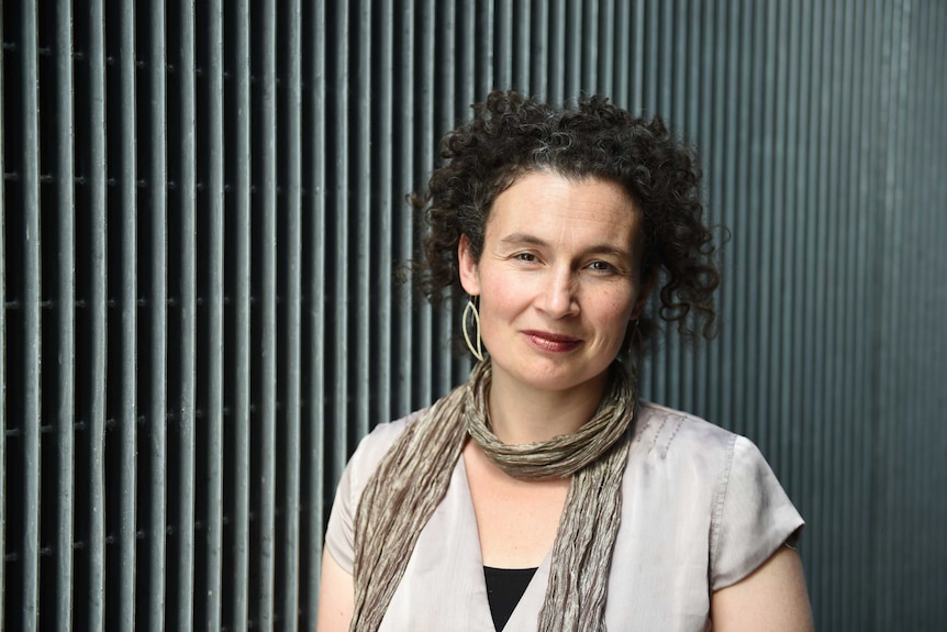 A woman with curly black hair standing in front of a corrugated wall.