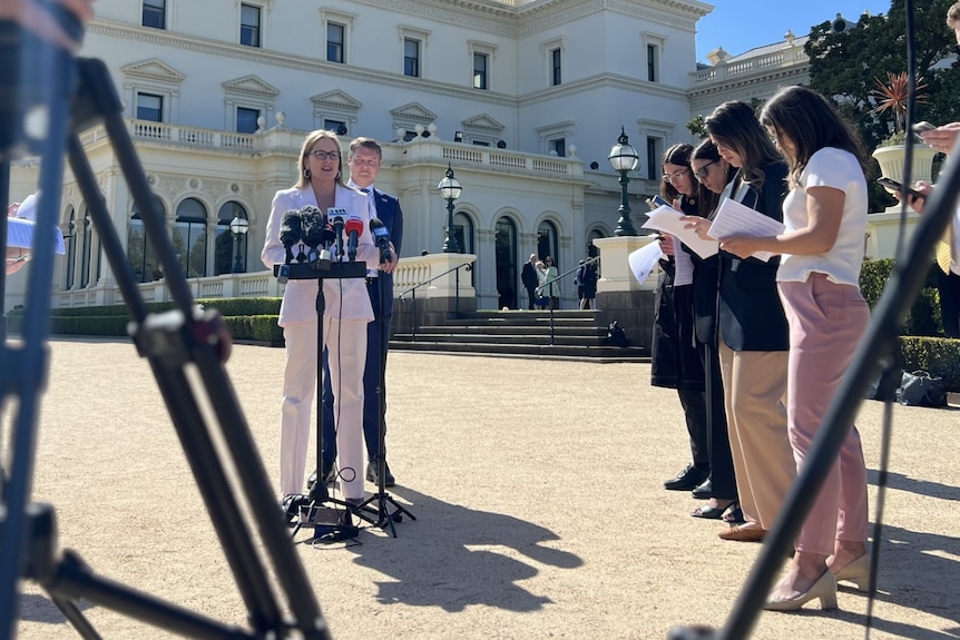 Jacinta Allan stands at a podium speaking to media with cameras pointed in her direction