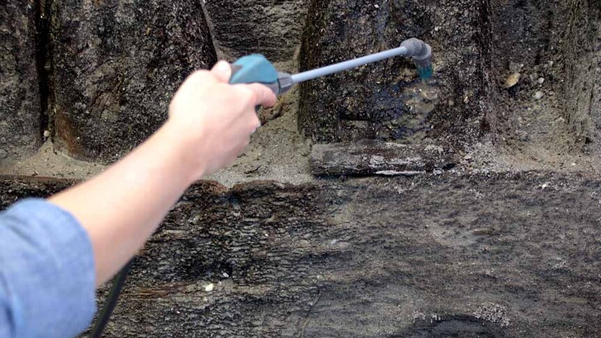 A handheld hose washes sand off timber