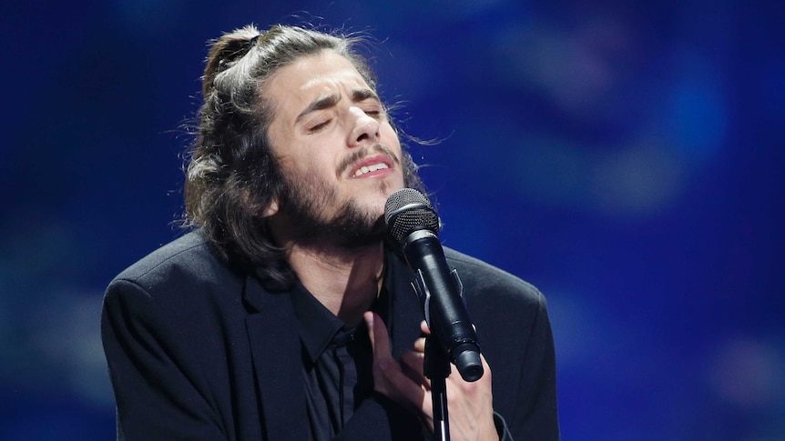 Portugal's Salvador Sobral holds his hands to his heart as he wears a black suit and shirt
