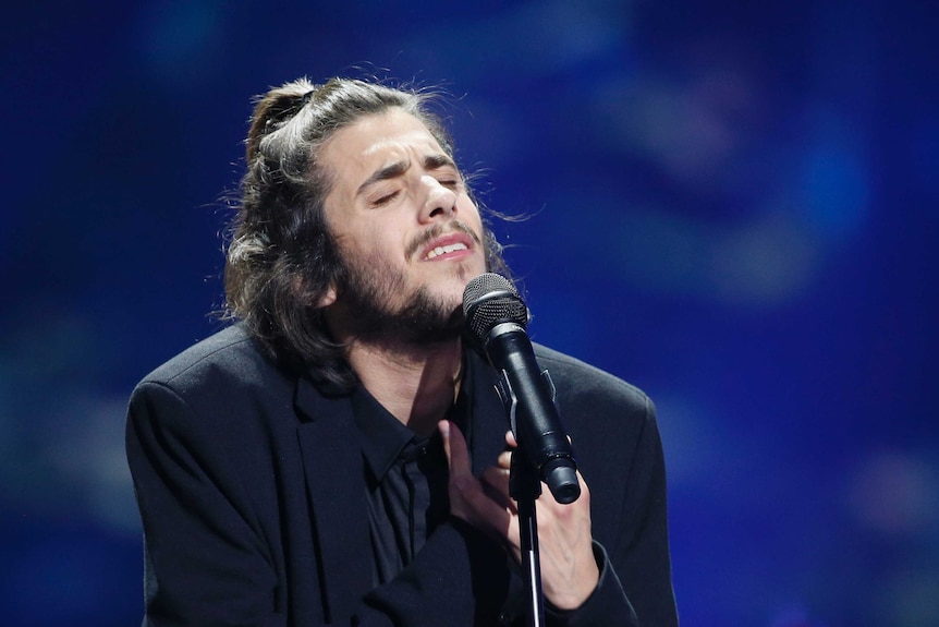Portugal's Salvador Sobral holds his hands to his heart as he wears a black suit and shirt