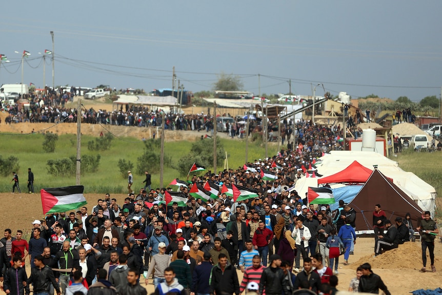 Thousands of Palestinians are seen walking with flags in a procession near the fence.