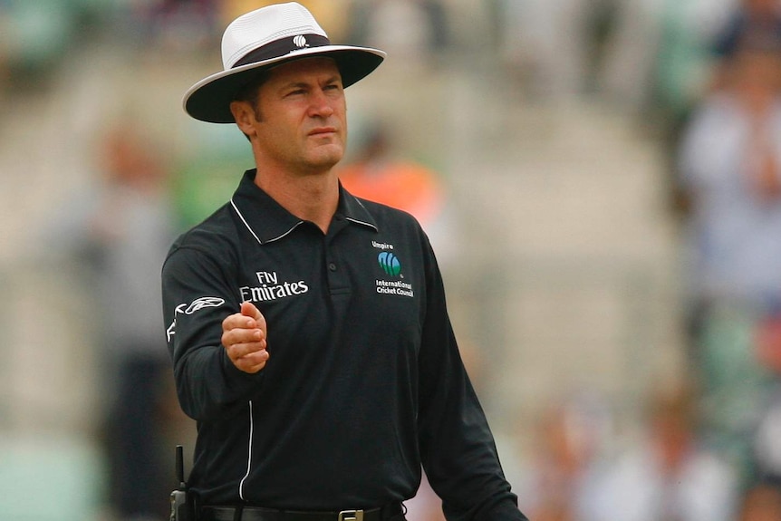 Simon Taufel is in all-black umpiring gear, holding a bowler's hat.