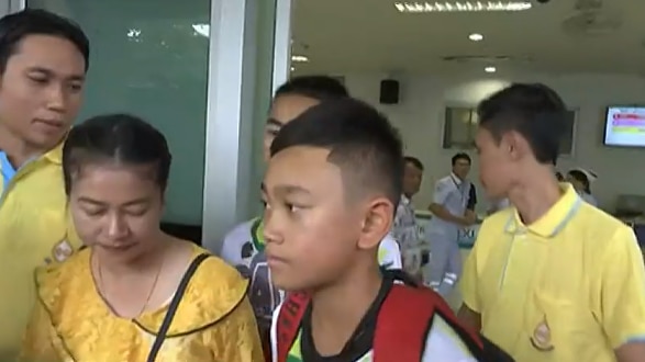 Close view of the face of a teen boy with a neutral expression, among a small group of people walking out of hospital in yellow