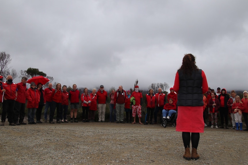 A line of people wearing red face a woman who has her back to the camera