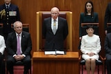 Hurley stands with a medal around his neck. He is flanked by Scott Morrison to his left, and his wife Linda on his right.