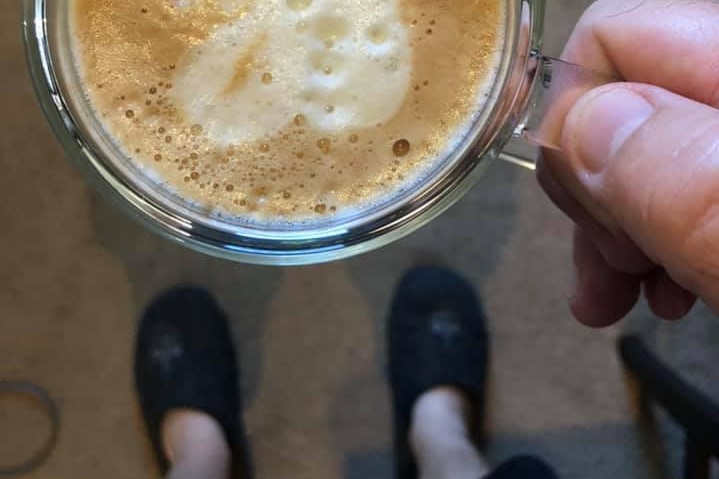 A man holds a cup of coffee while wearing a pair of slippers in his home.