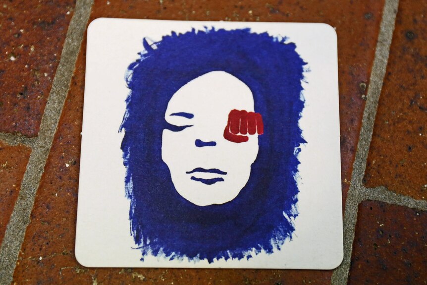 Coaster with a painted blue and white face and a red fist