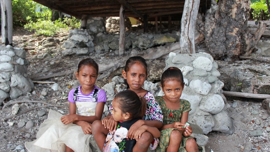 Four young girls sit on coral rocks on the beach at Atauro Island, East Timor