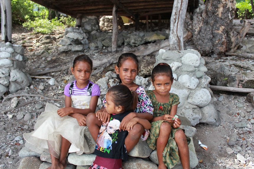 Four young girls sit on coral rocks on the beach at Atauro Island, East Timor