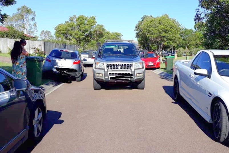 A 4WD carefully drives through a tight street lined with parked cars.