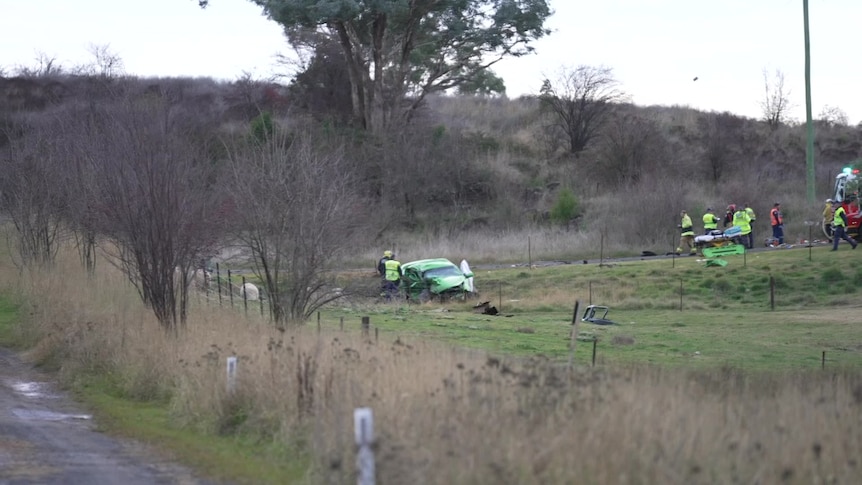 A green sedan crashed in a field, with emergency services attending 