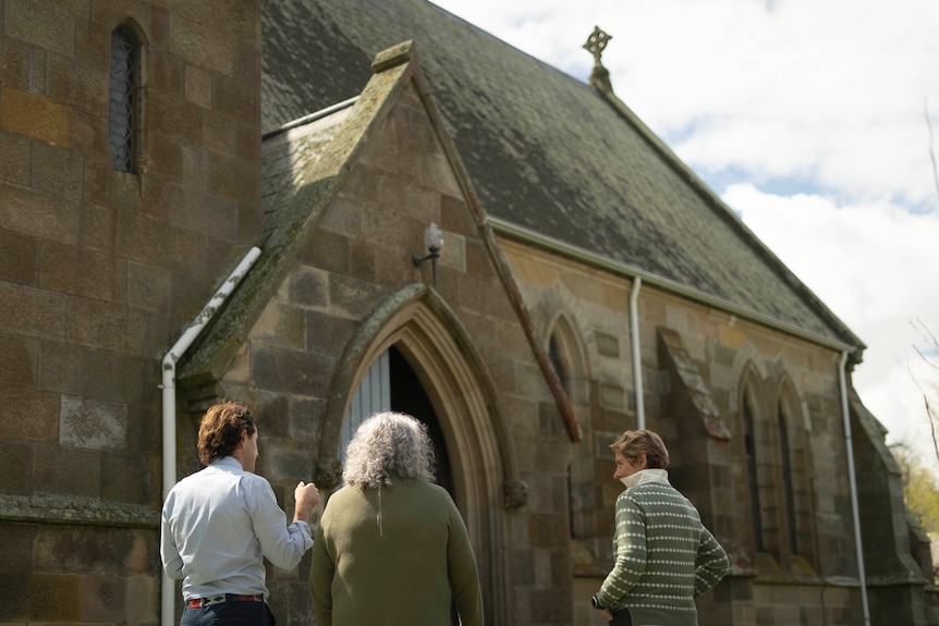Three people stand talking outside St John's church in Ross.