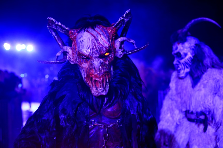 A man dressed as a goat like demon performs under unnerving blue light.