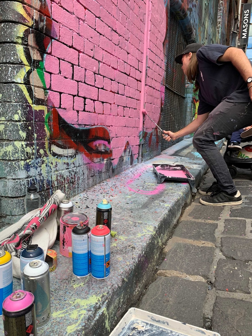 Man paints a brick wall pink with a small roller.