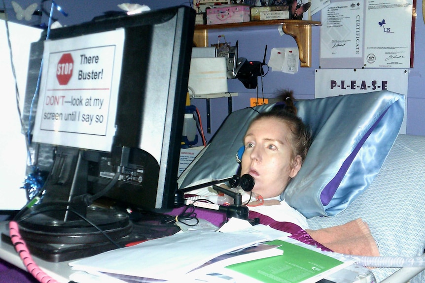 A woman lies in a bed in front of a screen with a message on the back which says, 'stop there buster! Don't look at my screen.