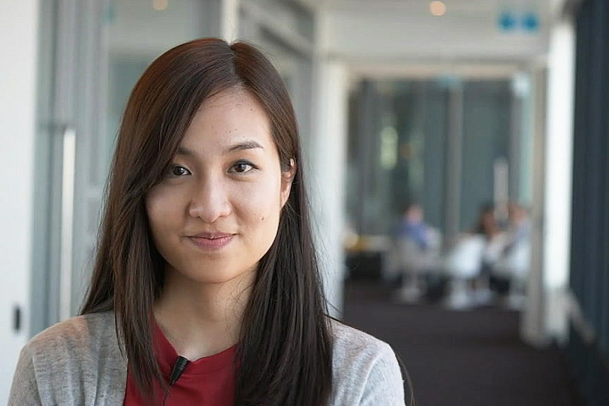 A woman smiles at the camera in an office corridor